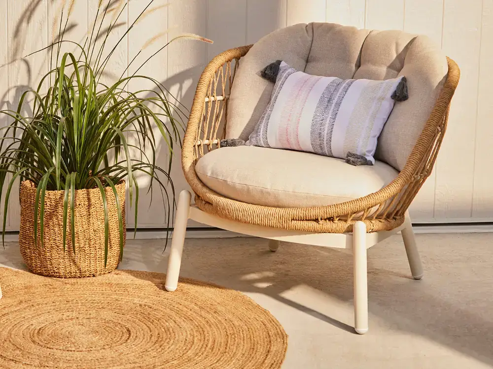 Fauteuil Kaya en rotin crème avec coussin brodé sur une terrasse.